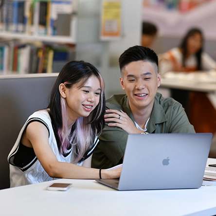 2 smiling students using a laptop.